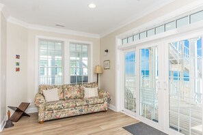 Un salon avec un canapé à motifs floraux, une lampe et une vue sur un balcon aménagé avec du mobilier d’extérieur.