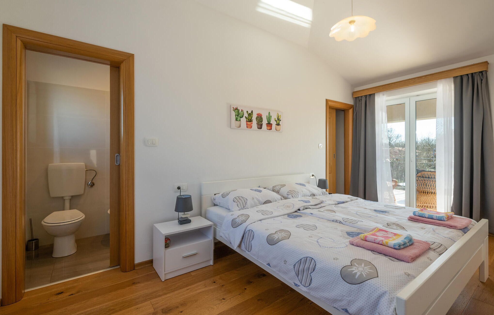 Quarto com cama, mesa de cabeceira e janela com cortinas.