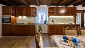 A kitchen with wooden cabinets, a stove, and a sink. There is a dining table with chairs and a bed with a floral bedspread. - Gorgeous home in Nedescina (Nedescina)