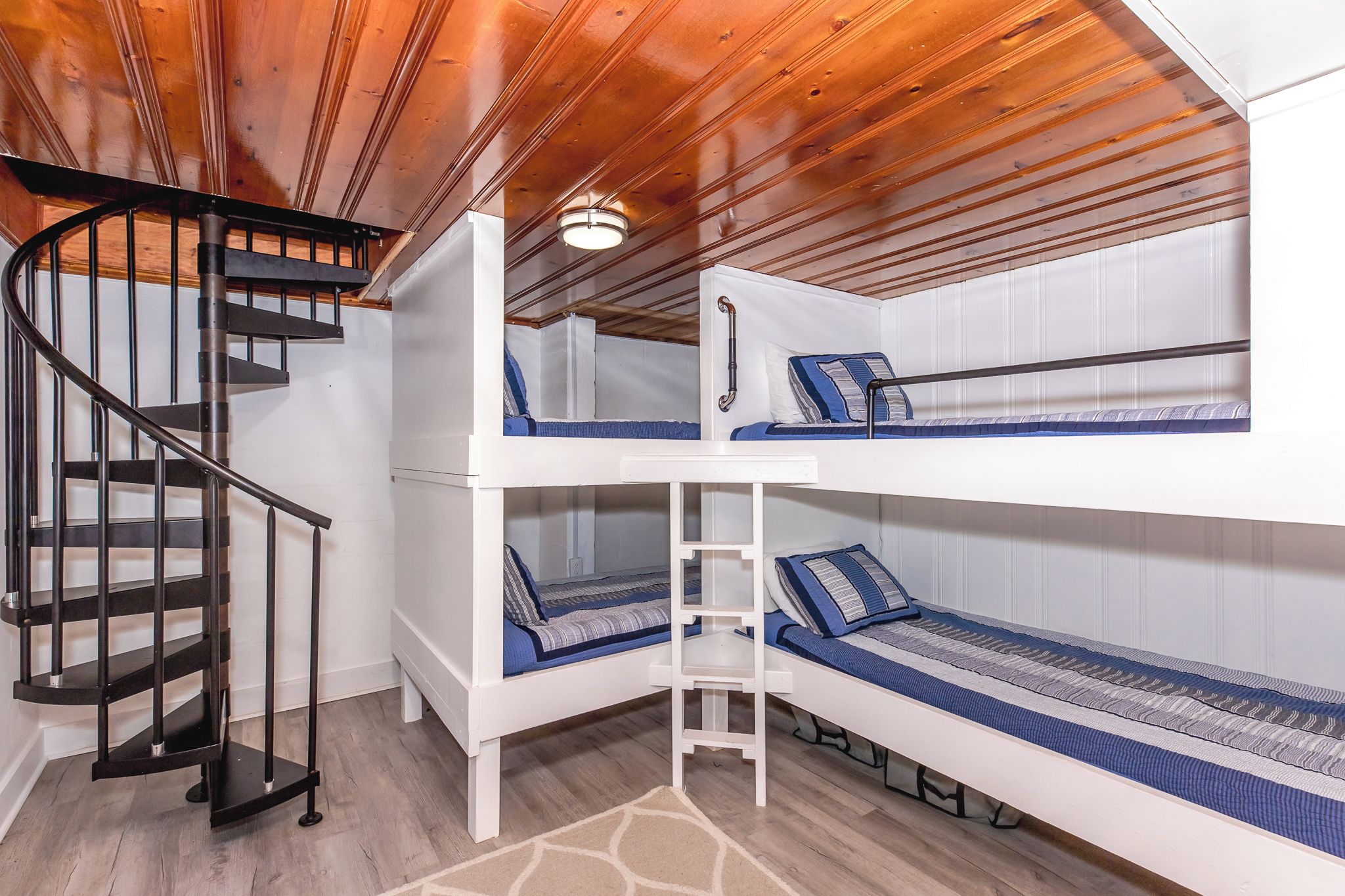 A bunk bed room with a spiral staircase and a wooden ceiling.