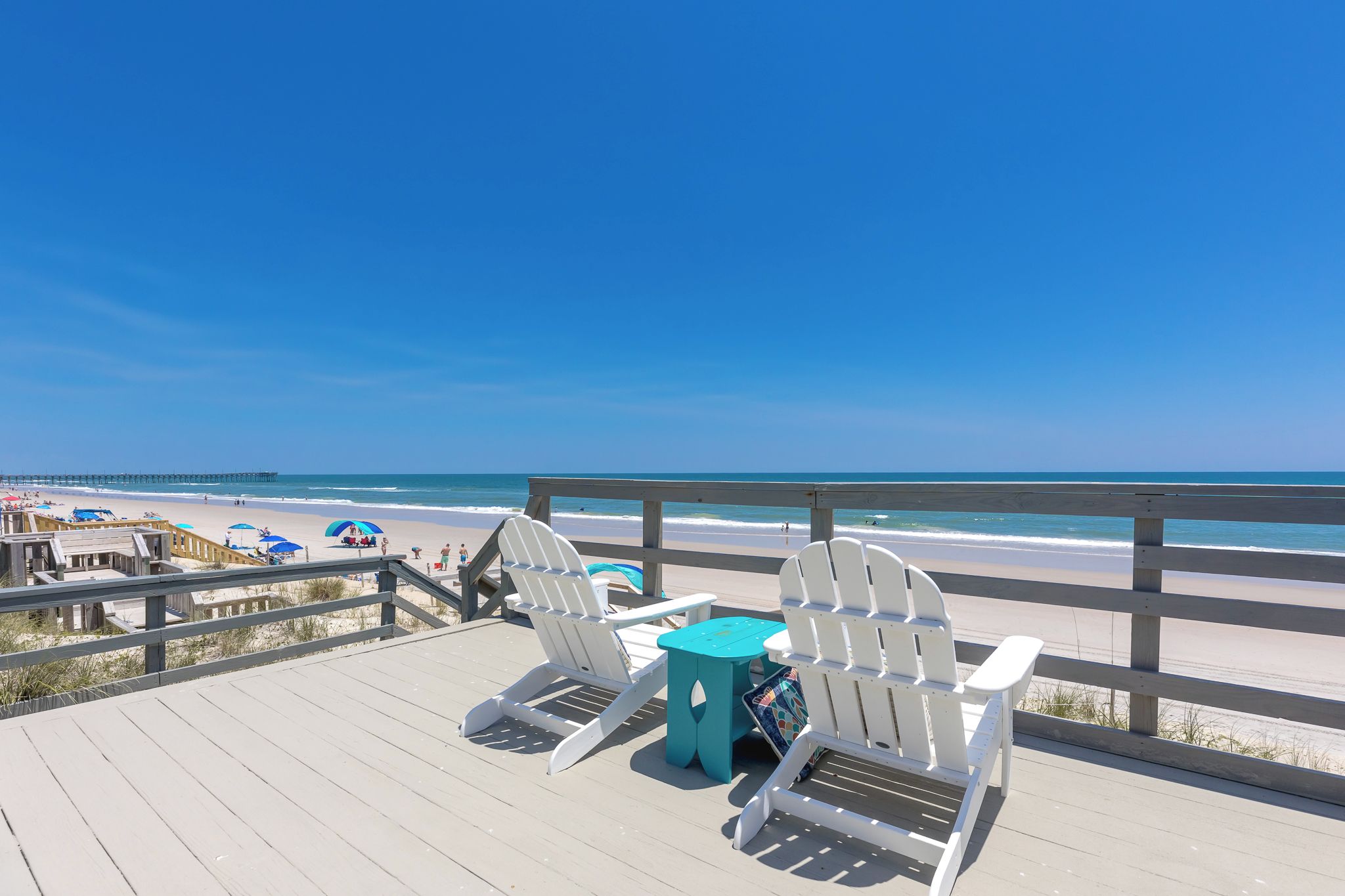 A beachside deck with two Adirondack chairs and a small table, overlooking a sandy beach and the ocean.
