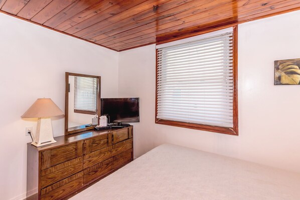 A bedroom with a wooden dresser, a television, a lamp, and a window with blinds.