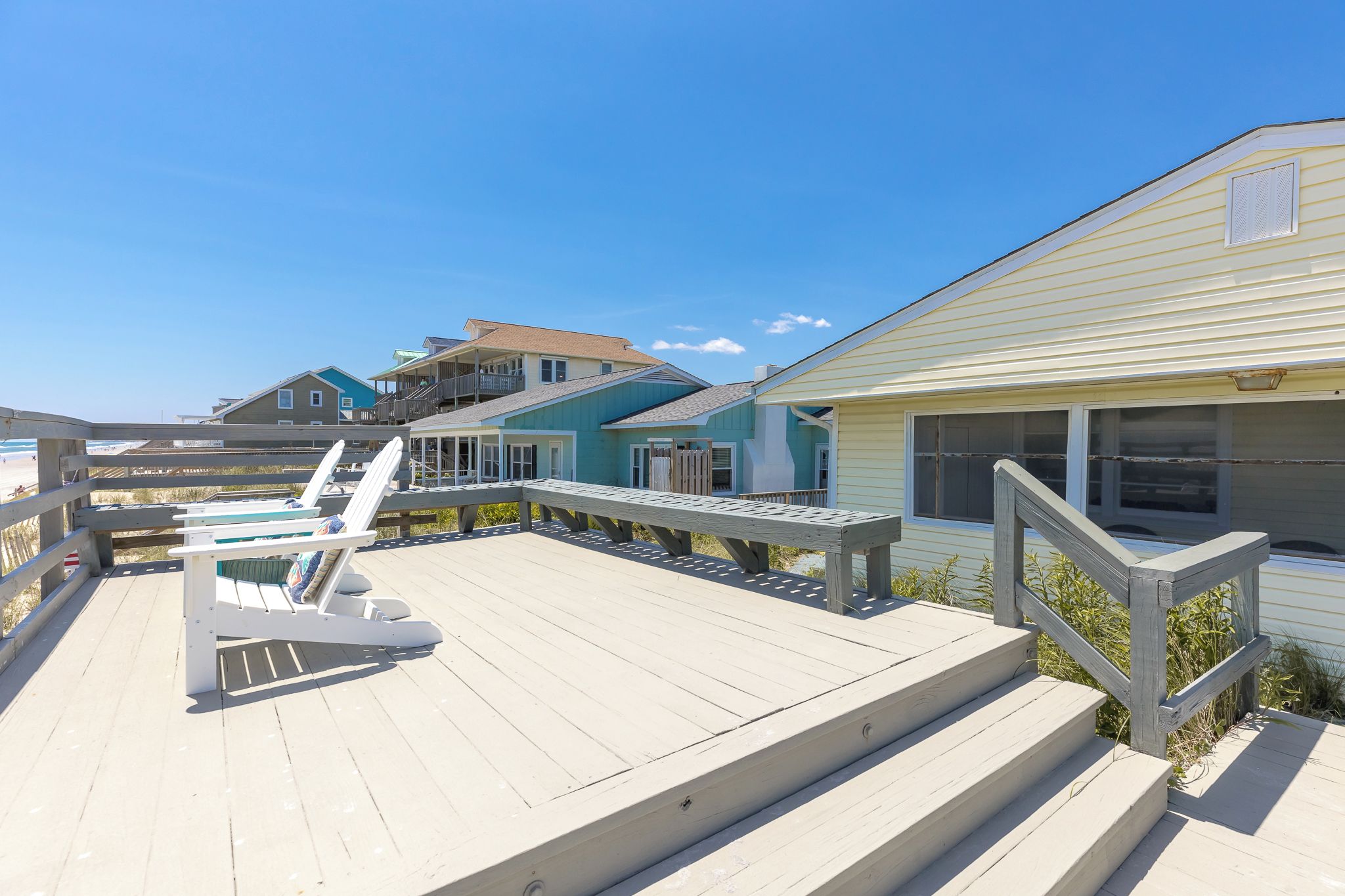 Une propriété située en bord de mer, comprenant plusieurs maisons, une terrasse en bois et un escalier menant à la plage.