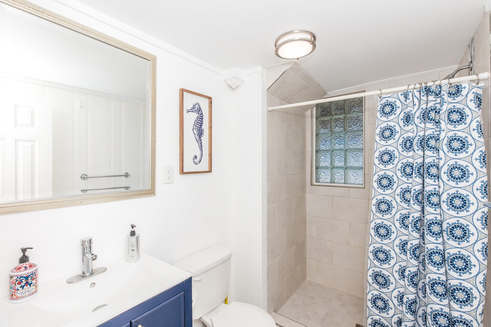 A bathroom with a large mirror, a framed seahorse artwork, a shower with a patterned curtain, and a toilet.