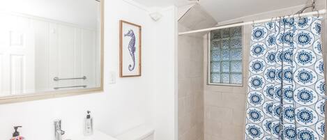 A bathroom with a large mirror, a framed seahorse artwork, a shower with a patterned curtain, and a toilet.