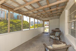 A covered porch with a view of the outside, a table with chairs, and a window with blinds.