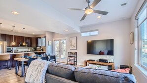 A modern kitchen with dark wooden cabinets, a dining area with a gray sofa, and a large flat-screen TV. - Modern Townhouse - Walkable to Mile High Stadium - Rooftop Views with Firepit (Denver)