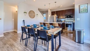 A modern kitchen with wooden cabinets, stainless steel appliances, and a dining area with a wooden table and black chairs. - Modern Townhouse - Walkable to Mile High Stadium - Rooftop Views with Firepit (Denver)