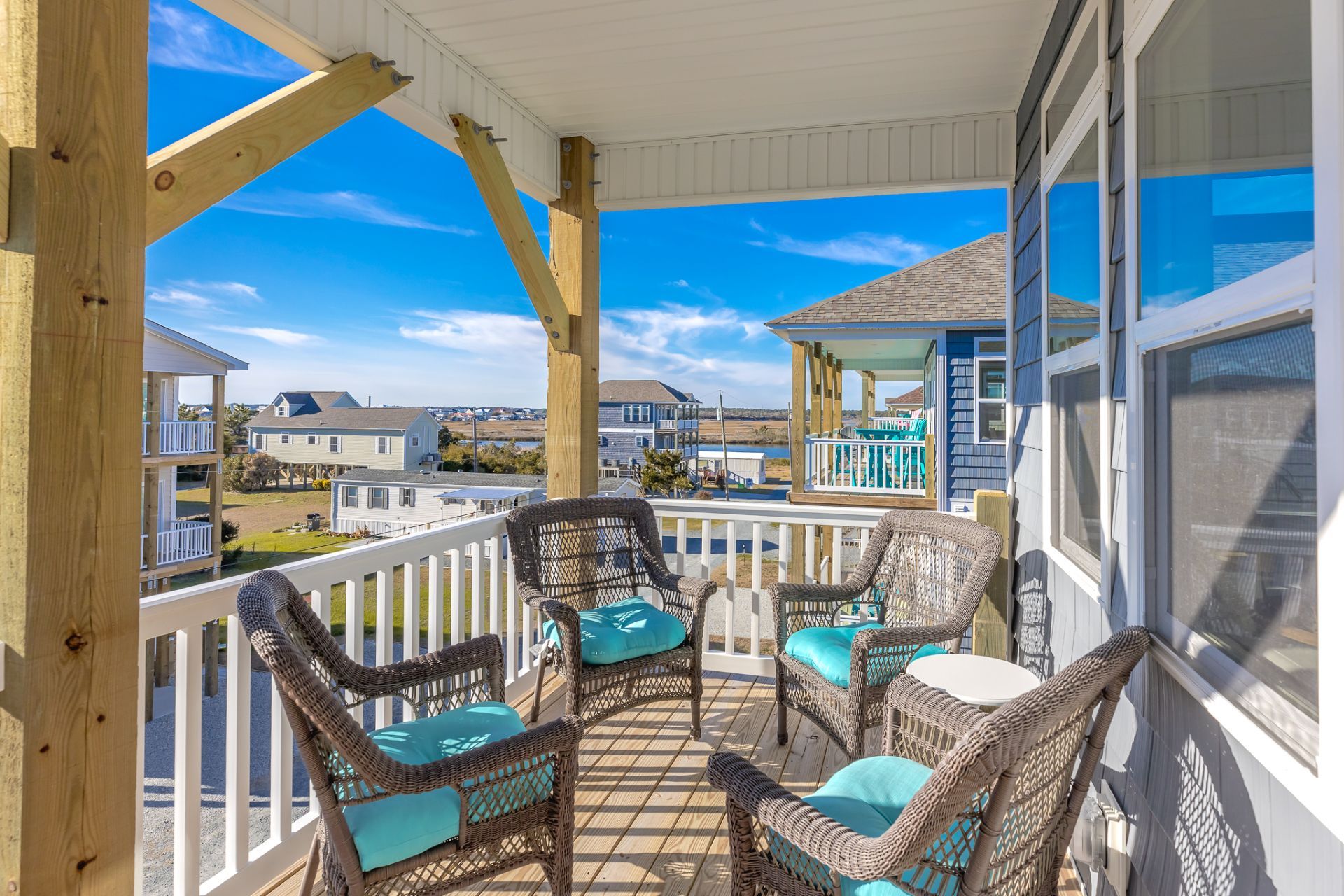A wooden deck with wicker chairs and a table, overlooking a residential area and a body of water.