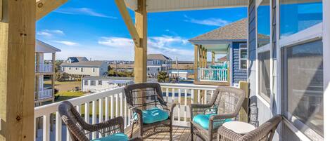 A wooden deck with wicker chairs and a table, overlooking a residential area and a body of water.