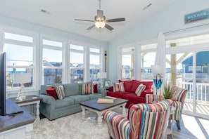 A spacious living room with a large window, a ceiling fan, and a view of the beach.