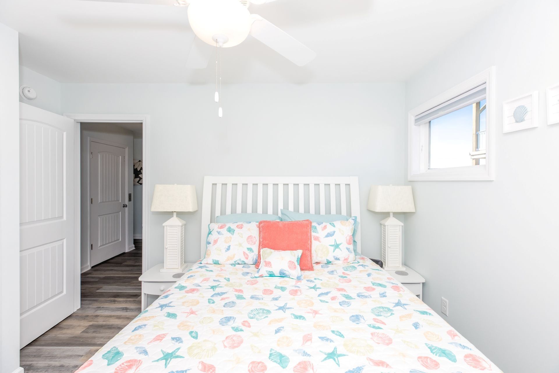 Une chambre à coucher avec un lit, deux tables de chevet, un ventilateur de plafond et une fenêtre.