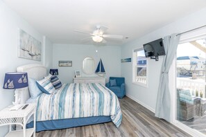 A bedroom with a bed, a chair, a dresser, a ceiling fan, a TV, and a window with a view. - The Country Crab - 4BR Home, Elevator, Pet Friendly! (North Topsail Beach)
