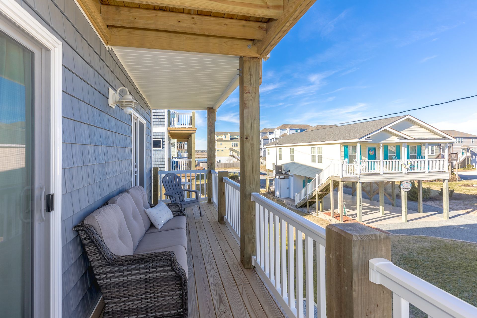 A wooden deck with a white railing, a wicker sofa, and a view of neighboring houses.