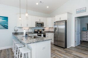 A modern kitchen with white cabinets, a stainless steel refrigerator, a microwave, and a granite countertop. - The Country Crab - 4BR Home, Elevator, Pet Friendly! (North Topsail Beach)