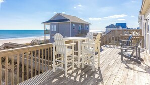 Une terrasse en bois avec des sièges extérieurs, offrant une vue sur une plage et l’océan.