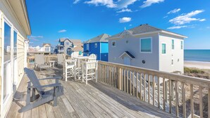 Une terrasse en bois avec des maisons de plage, une vue sur l’océan et un ciel dégagé.