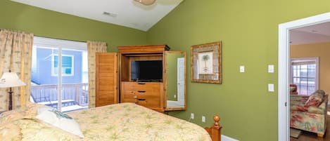 Un dormitorio con cama, televisor, armario y puerta que da a otra habitación.