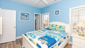 Une chambre à coucher comprenant un lit, un ventilateur de plafond, une porte, une fenêtre avec des stores et un tableau accroché au mur.