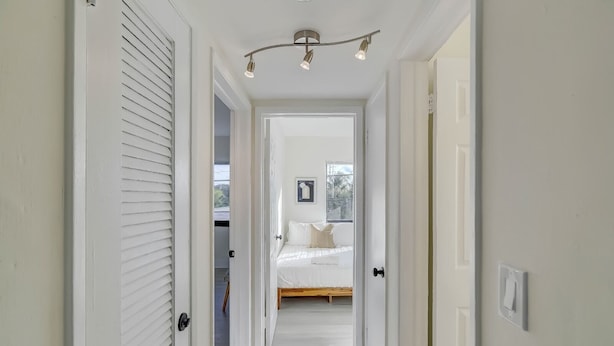 A hallway leading to a bedroom with a bed, a ceiling light fixture, and a window with a view. - Modern & Rlx space for 6 ppl (Fort Lauderdale)
