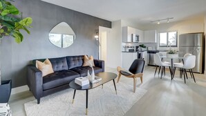 A modern living room with a dark sofa, a coffee table, and a dining area with a white table and chairs. - Modern & Rlx space for 6 ppl (Fort Lauderdale)