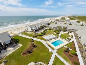 Vista aérea de um hotel à beira-mar com piscina, acesso direto à praia e um gramado bem cuidado.