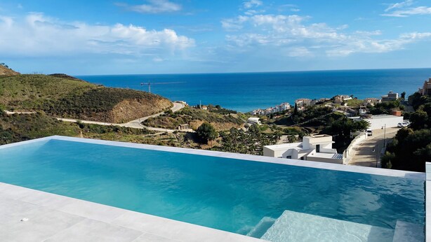 A swimming pool with a view of the sea and a hilly landscape.