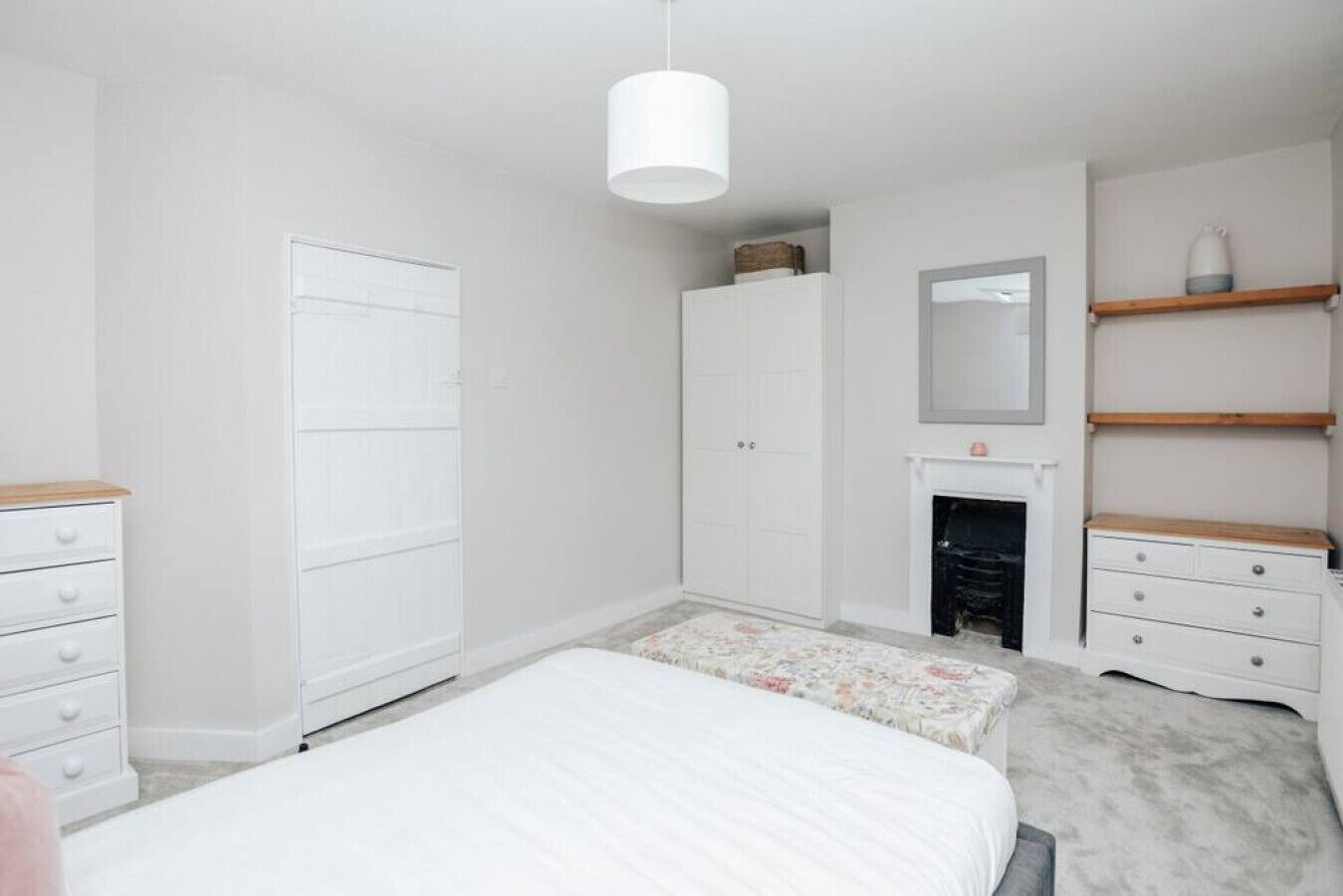 Un dormitorio con cama, armario, cómoda, espejo y chimenea.