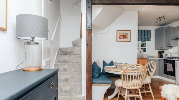 A cozy dining area with a round table and wooden chairs, a staircase leading to another level, and a kitchen with grey cabinets.