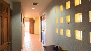 Ein Flur mit Fliesenboden, einer Tür links und einer Wand mit quadratischen Aussparungen rechts.