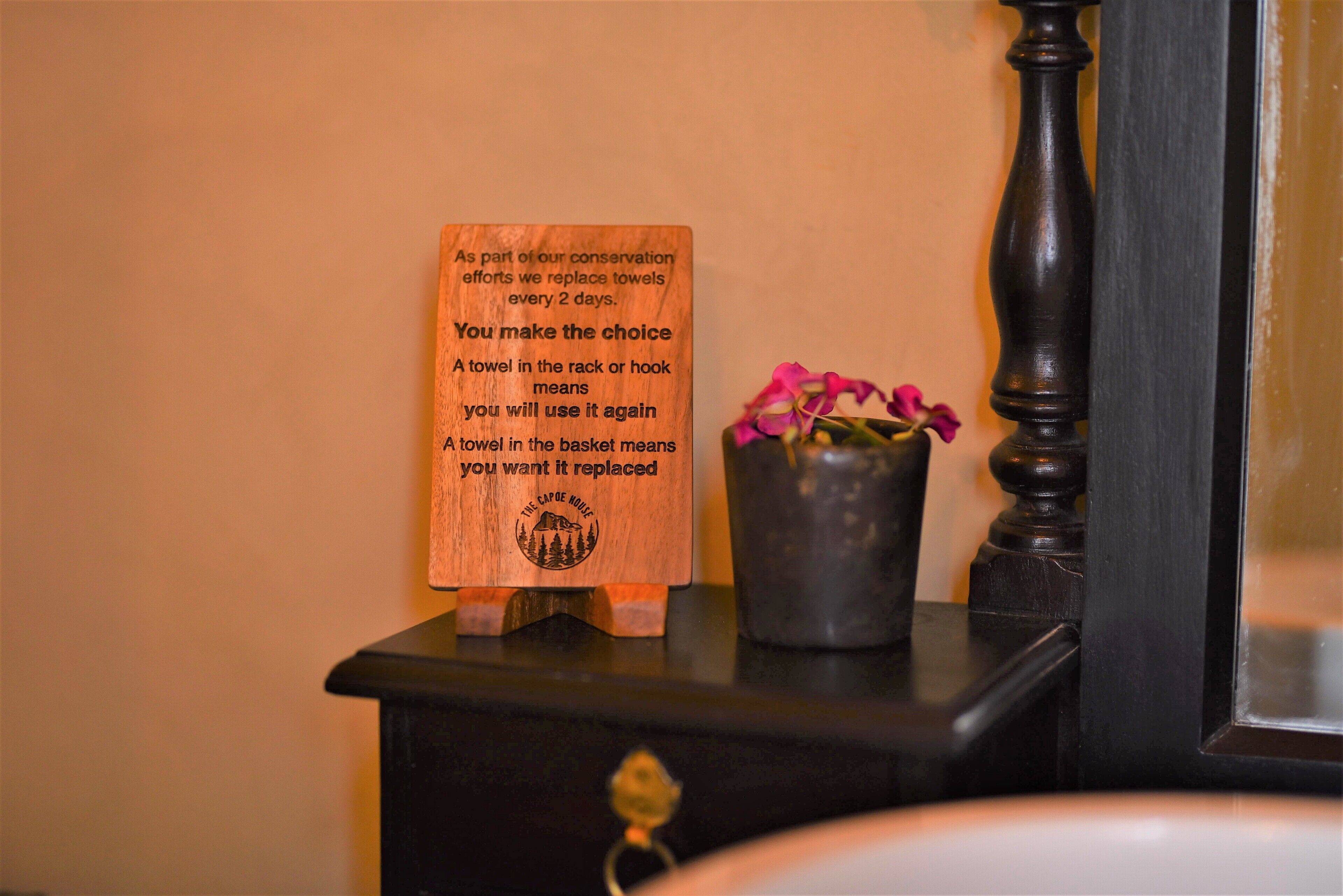 A wooden sign with conservation message, a small potted plant, and a dark wooden dresser.