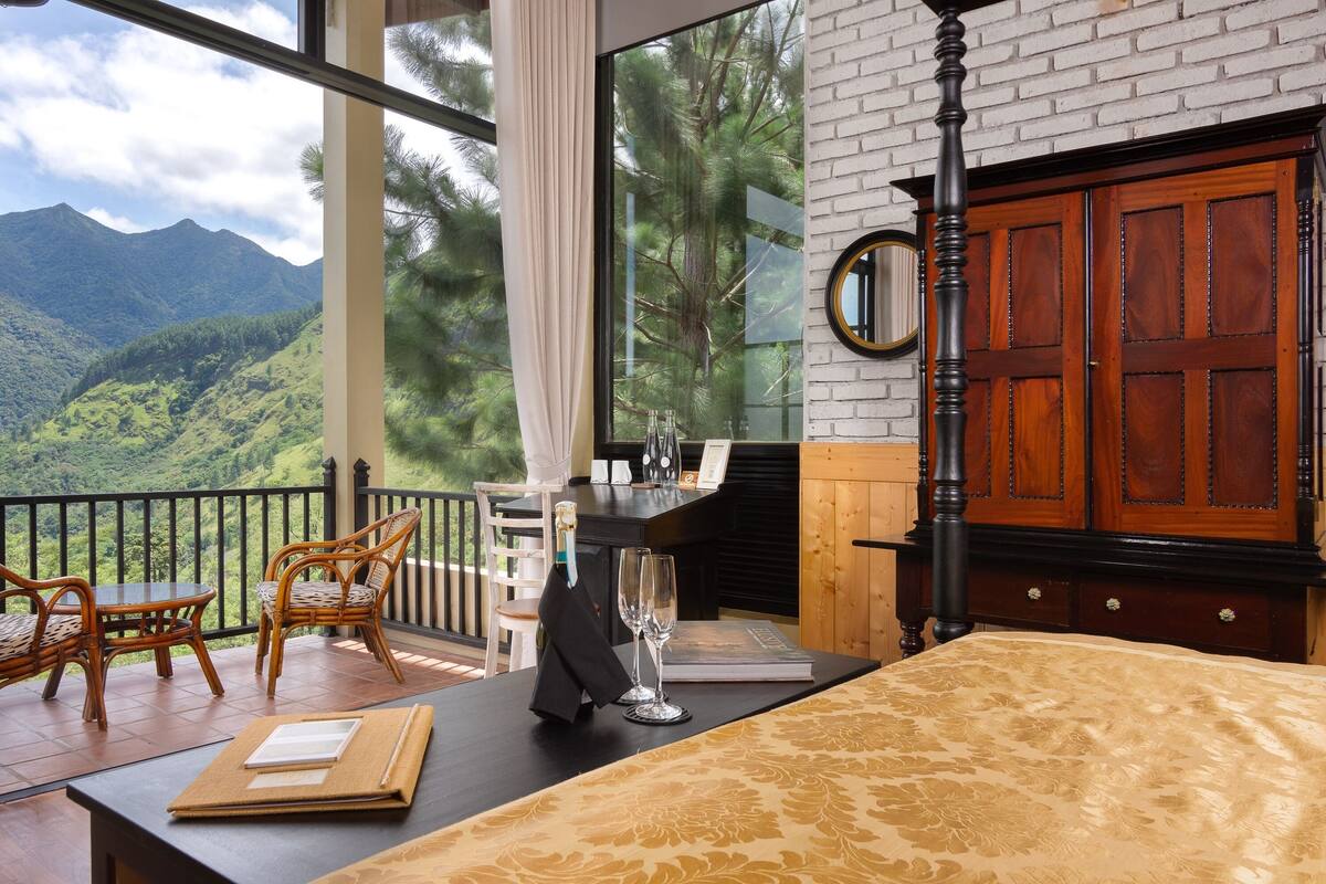 A balcony with wicker chairs, a table, and a view of mountains.