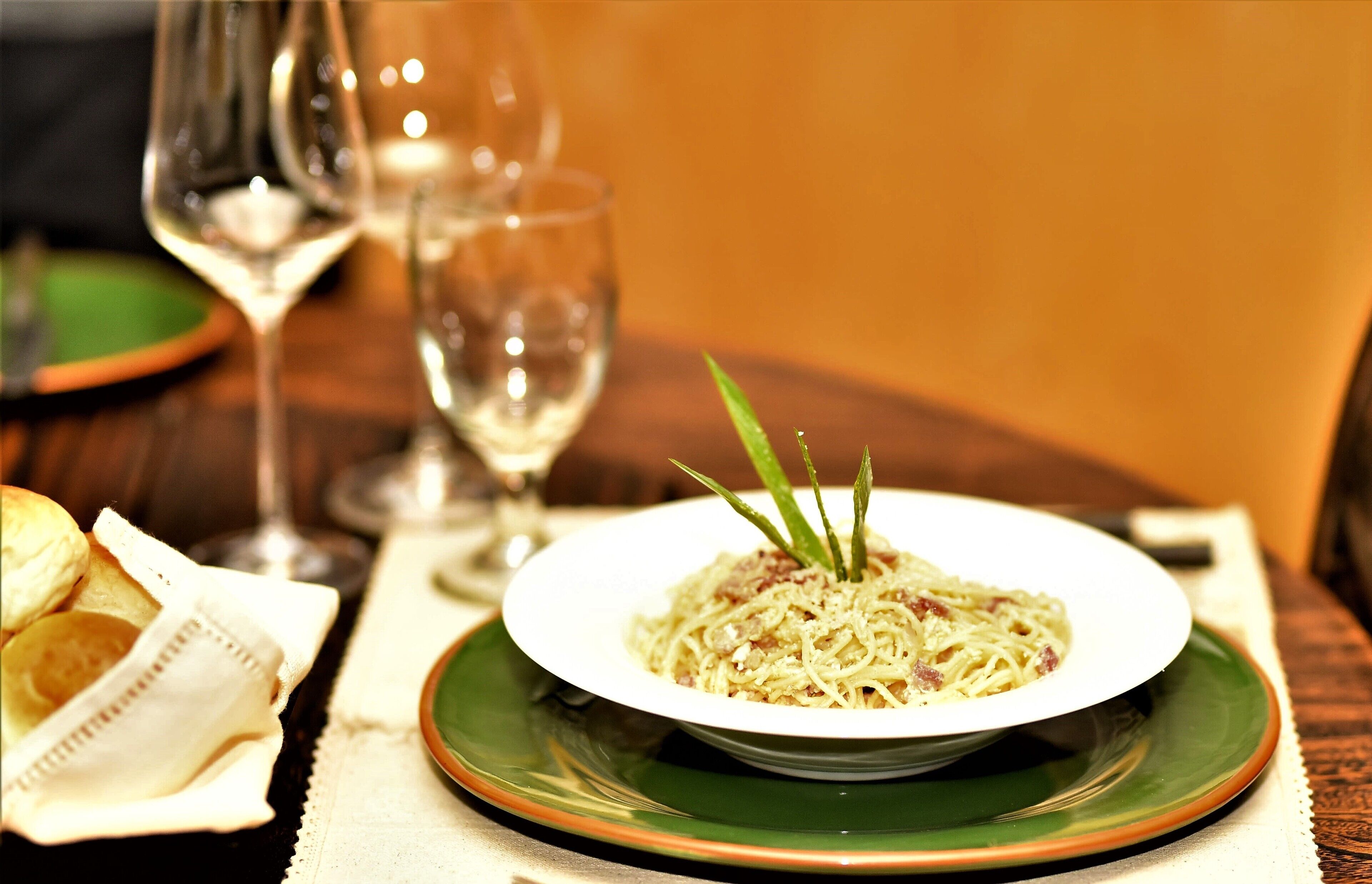 A plate of spaghetti garnished with green herbs, accompanied by a glass of white wine and a green plate on a table.