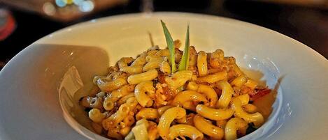 A white plate with a pasta dish, a glass of wine, and a blurred background with lights.