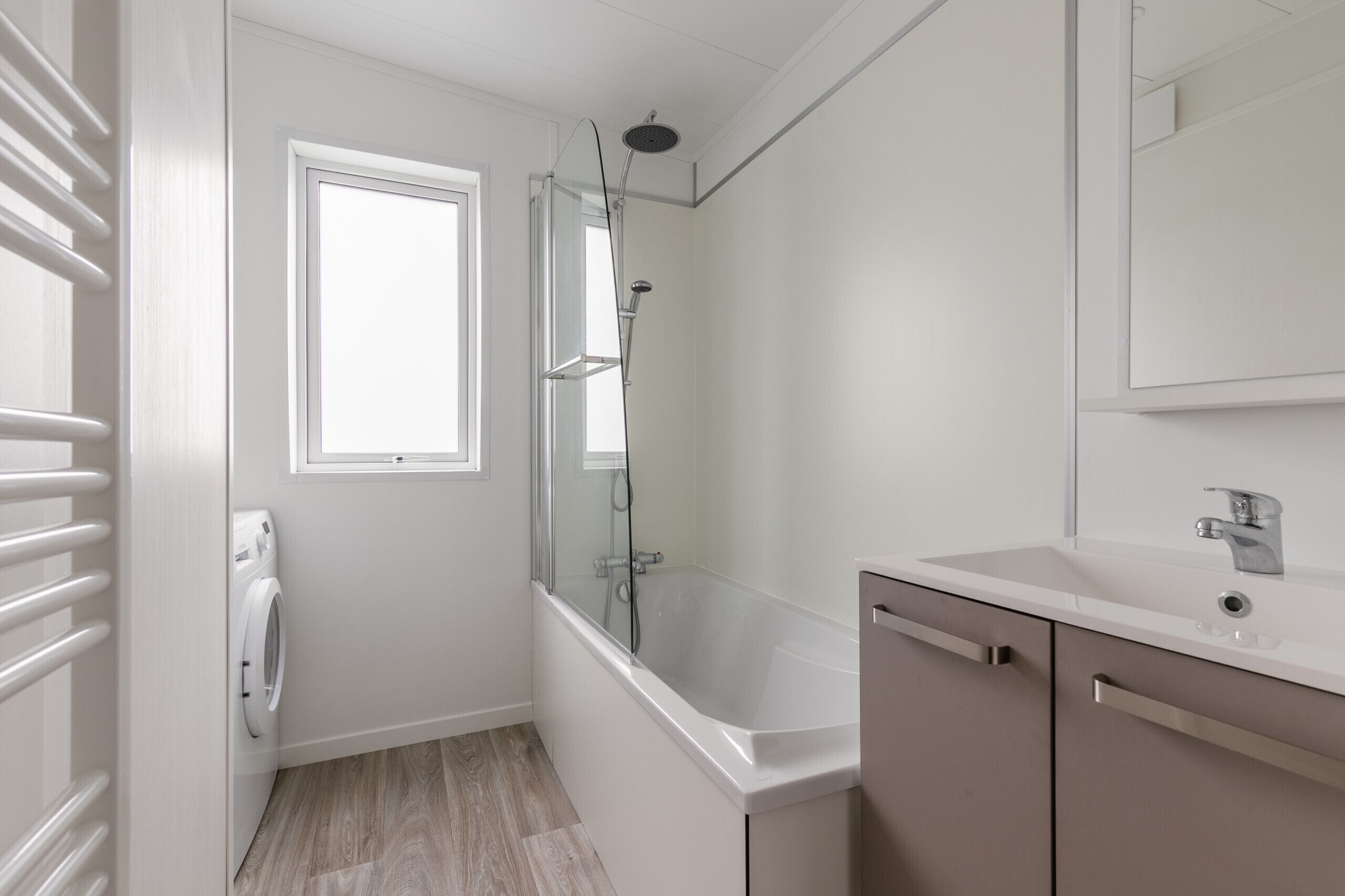 Une salle de bain moderne avec une douche à parois de verre, un lavabo blanc et un lave-linge encastré.