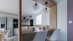A modern kitchen with a wooden island, white chairs, and pendant lights. - Beautiful Chalet for 4 people - Heated pool access (Bretignolles-sur-Mer)