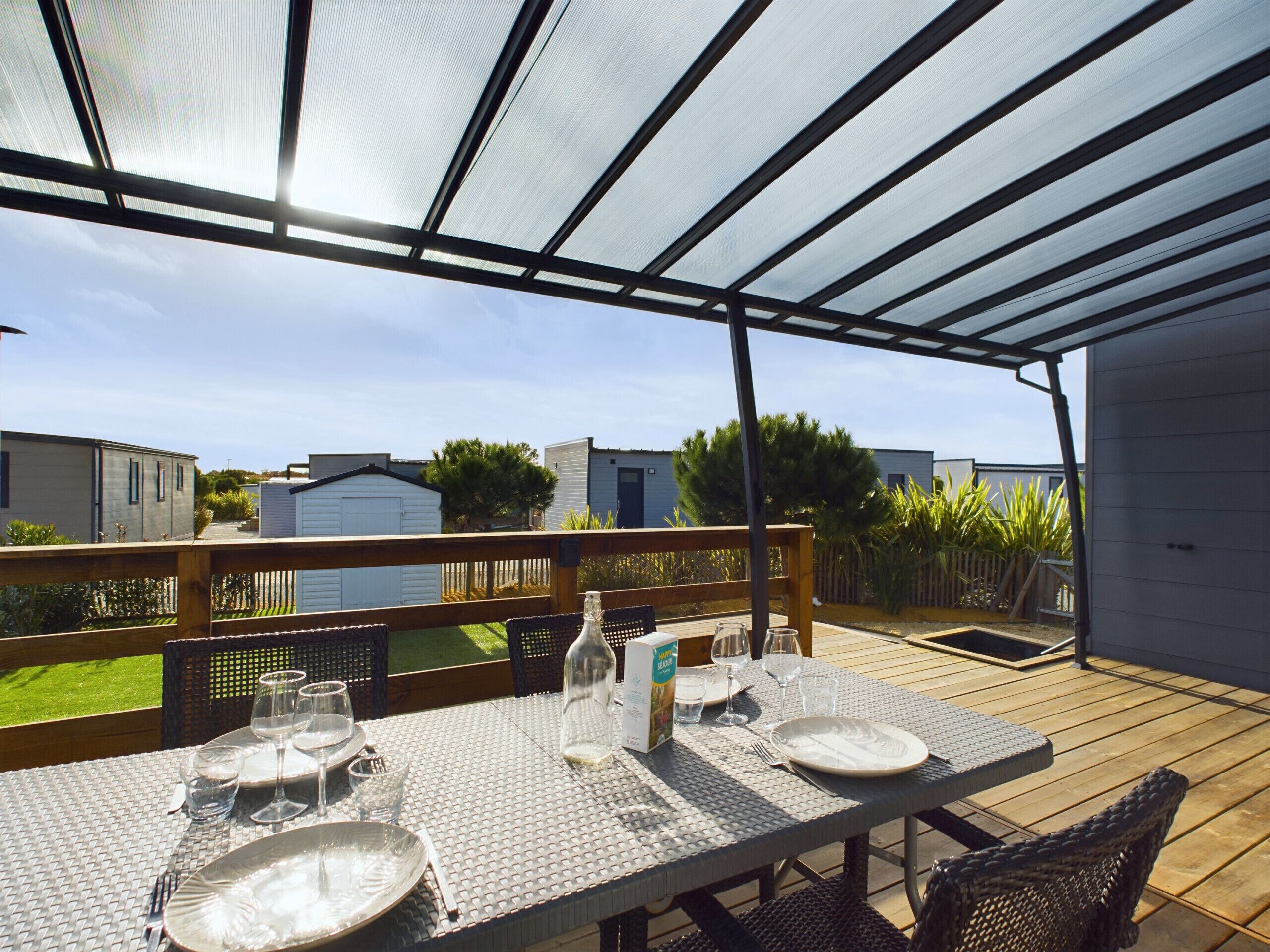 A covered outdoor dining area with a table set for four, surrounded by a wooden deck and a metal railing.