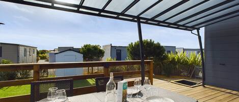 A covered outdoor dining area with a table set for four, surrounded by a wooden deck and a metal railing.