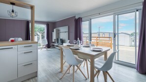 A modern kitchen with a wooden countertop, white cabinets, and a dining area with a wooden table and chairs. - Beautiful Chalet for 4 people - Heated pool access (Bretignolles-sur-Mer)