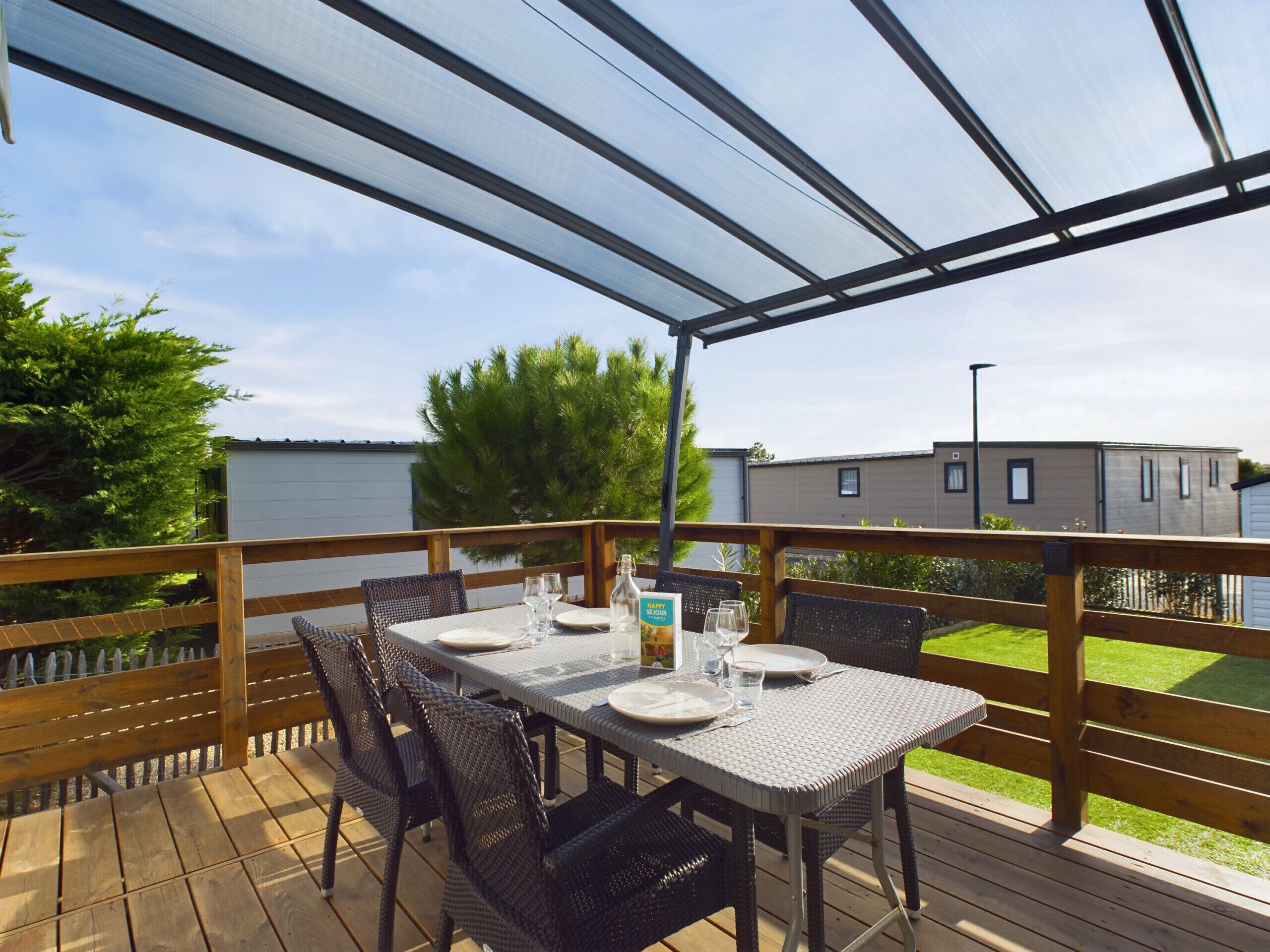 Een overdekte eethoek buiten, met een tafel gedekt voor twee personen, omringd door rieten stoelen, onder een transparant dak.