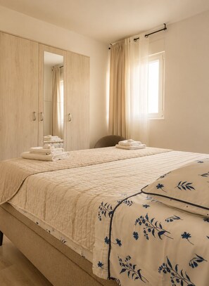 A bedroom with a bed, a mirror, a wardrobe, and a window with curtains.