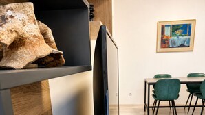 Une chambre moderne avec un téléviseur à écran plat posé sur un meuble en bois, un coin repas avec des chaises vertes et un tableau accroché au mur.