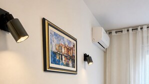 Un salon comprenant un canapé, un tableau encadré, des lampes fixées au mur et un appareil de climatisation.