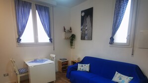 A room with a blue sofa, a white desk, and a window with blue curtains. - B&BO - IN BOLOGNA YOU DREAM - APARTMENT - FREE PARKING  (BOLOGNA)