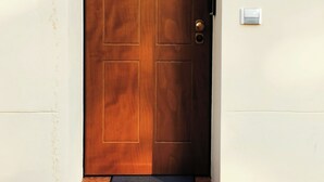 A wooden door with a simple design, a wall-mounted light above it, and a thermostat on the wall to the right. - B&BO - IN BOLOGNA YOU DREAM - APARTMENT - FREE PARKING  (BOLOGNA)
