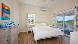 A bedroom with a bed, a nightstand, a dresser, a window with curtains, an air conditioning unit, and a balcony with a view of greenery.