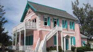 A pink building with white balconies and green shutters, featuring a staircase and a porch.
