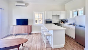 A modern kitchen with white cabinetry, a central island with bar stools, a built-in microwave, and a refrigerator.