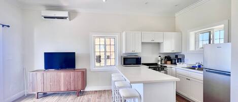 A modern kitchen with white cabinetry, a central island with bar stools, a built-in microwave, and a refrigerator.