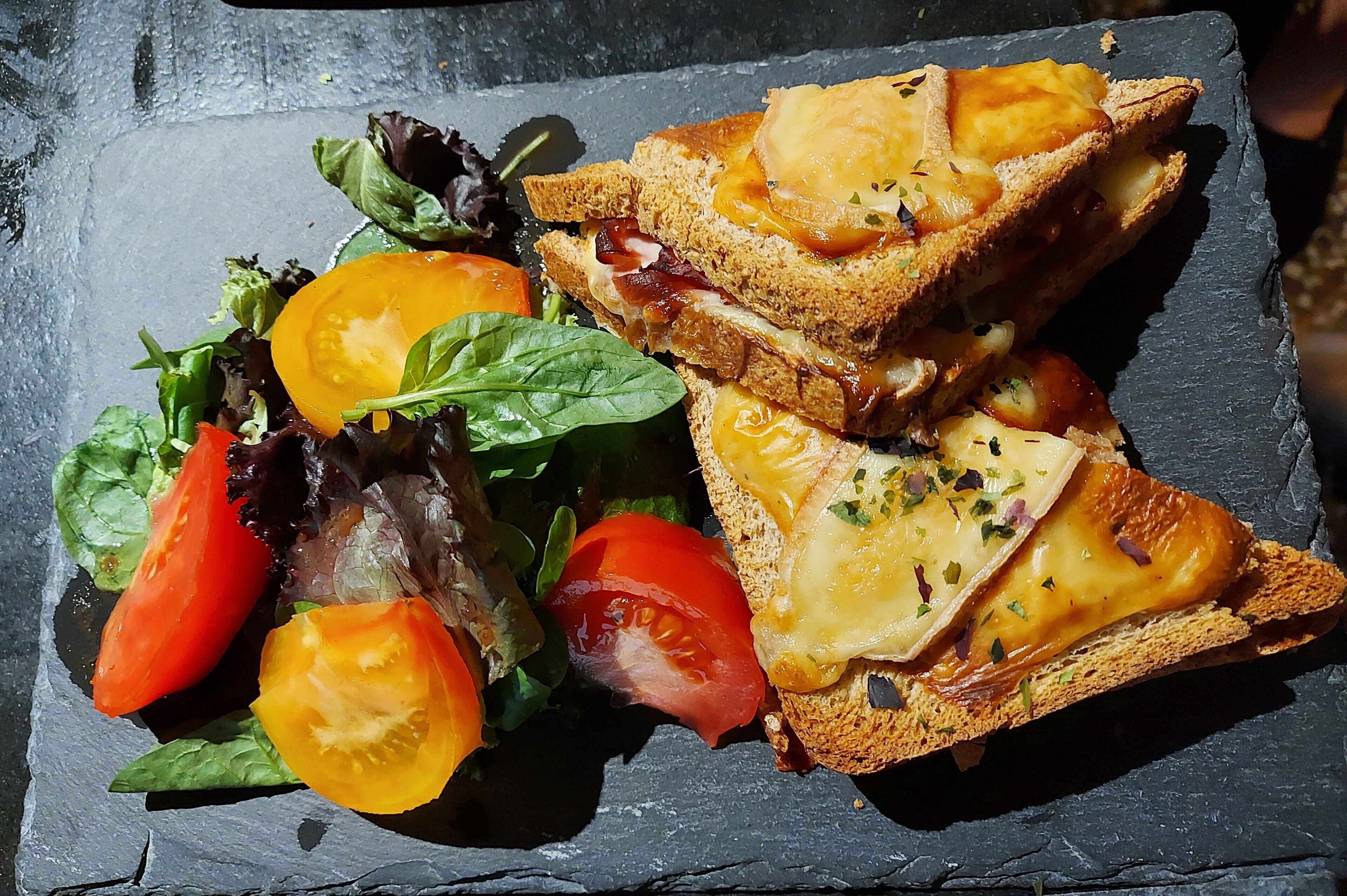 A sandwich with cheese and tomato slices on a slate plate.